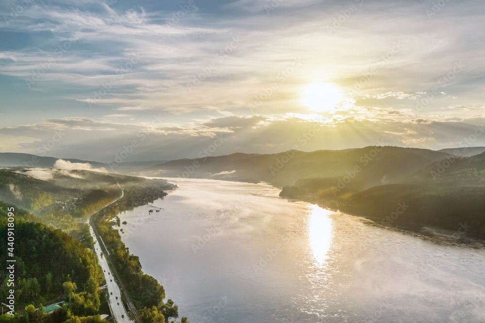 sunset on the river, evening sun illuminates the hills and the road along the river, aerial view