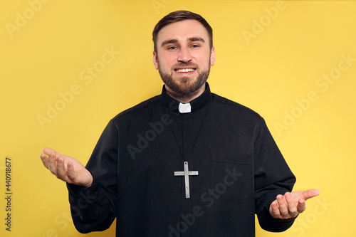 Priest wearing cassock with clerical collar on yellow background