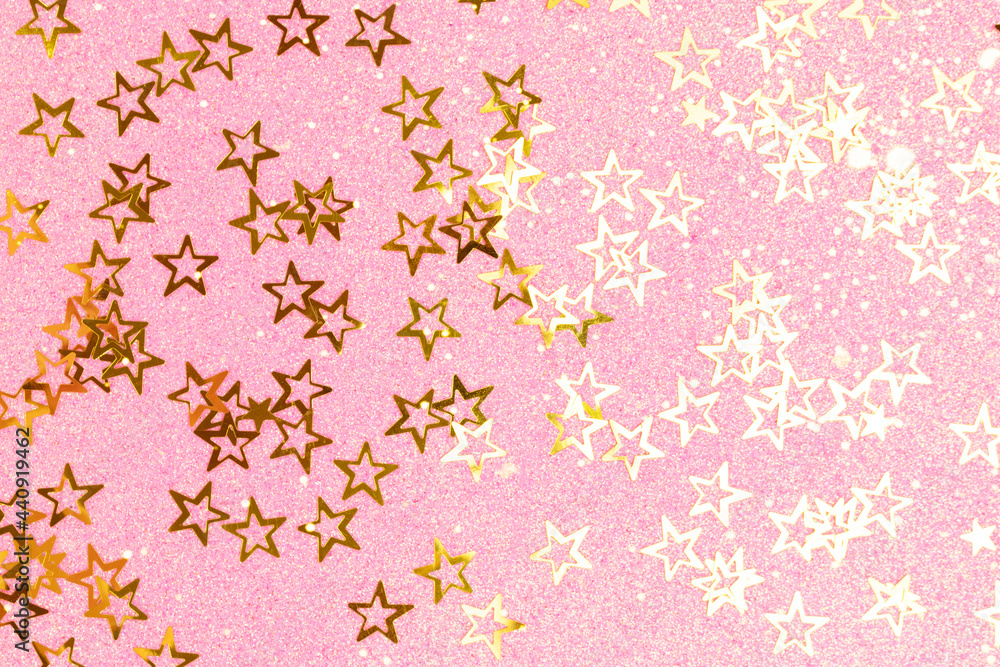 Shiny gold colored glittering stars confetti scattered on a pink textured background.
