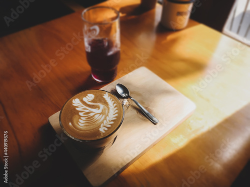 A cup of cappuccino with latte art swan design on wooden table background in a coffee shop. Top view of a cup of coffee with the afternoon sun shining through the window. Dark tone and vintage image.