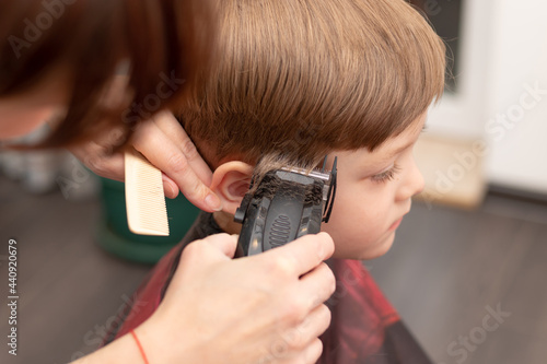 young mom hairdresser cuts her baby boy at home with hair clipper during quarantine. selective focus. portrait