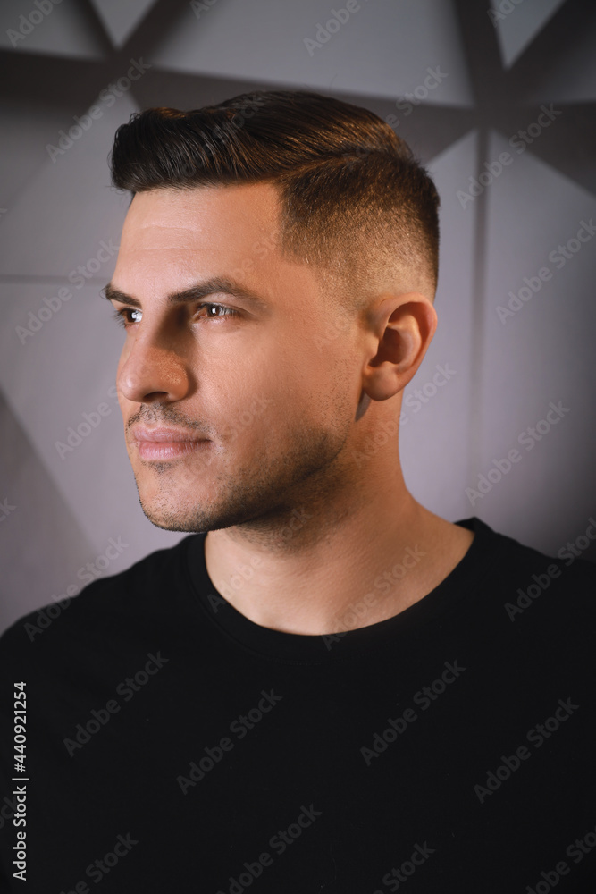 Fototapeta premium Handsome man with trendy hairstyle near dark wall