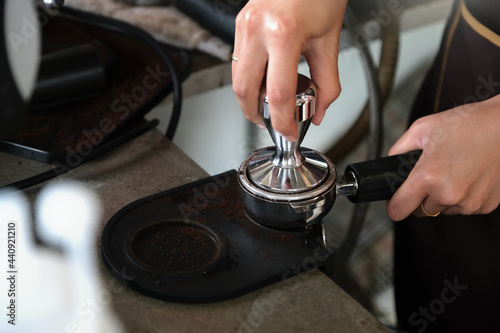 A female worker uses a tamper rod to press roasted coffee beans before they are put into the coffee machine