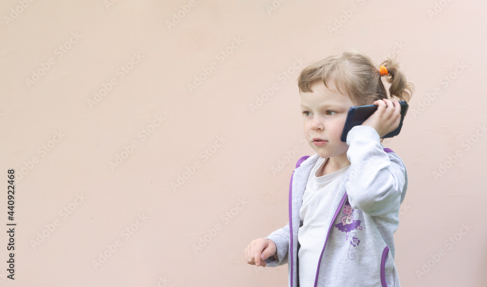 Little Caucasian child girl of five years old, curly blonde girl with a phone in her hands. The concept of child addiction to gadgets. Little Caucasian child girl of five years old, curly blonde girl with a phone in her hands. The concept of child addiction to gadgets.