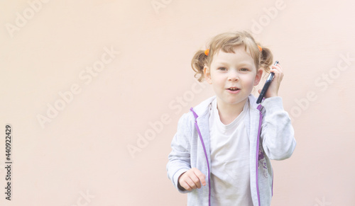 Little Caucasian child girl of five years old, curly blonde girl with a phone in her hands. The concept of child addiction to gadgets.