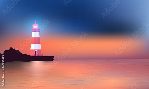 Beautiful sunset on ocean beach with the luminous Lighthouse standing on the embankment.