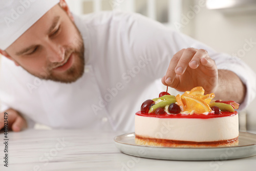 Happy professional confectioner decorating delicious cake at table in kitchen photo