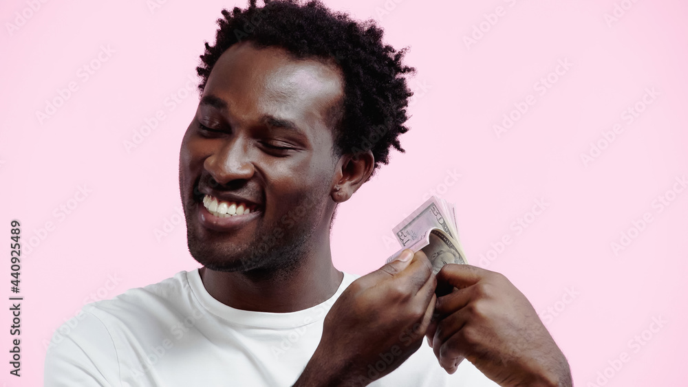 smiling african american man in white t-shirt holding dollars isolated on pink smiling african american man in white t-shirt holding dollars isolated on pink