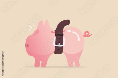 Tighten belt to reduce budget or spending, financial crisis or economic slow down, keep cost and expense low to survive, pink piggybank tighten belt on his belly metaphor of saving cost.