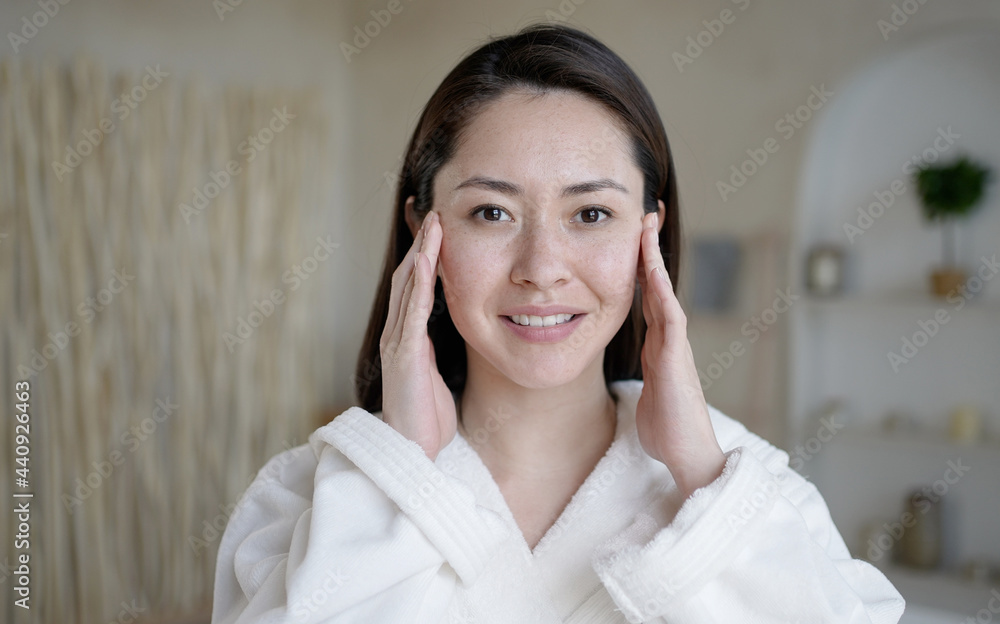 Attractive multi ethnic girl looking in mirror touching healthy soft face skin after daily treatment. Young mixed race asian woman doing massage satisfied with facial procedures skincare concept. Attractive multi ethnic girl looking in mirror touching healthy soft face skin after daily treatment. Young mixed race asian woman doing massage satisfied with facial procedures skincare concept.