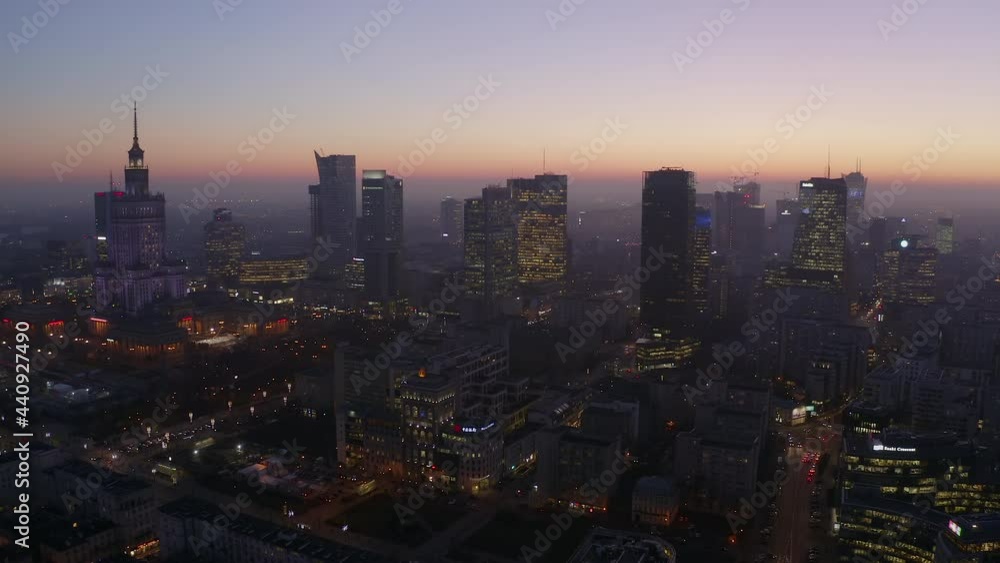 Drone view of the beautiful urban metropolis with skyscrapers and orange sky after sunset in the business center of Warsaw, Poland. The camera descends on a night city with night traffic and skyscrape Drone view of the beautiful urban metropolis with skyscrapers and orange sky after sunset in the business center of Warsaw, Poland. The camera descends on a night city with night traffic and skyscrape