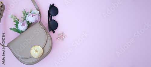 Business women's everyday-life travel accessories flat lay on pastel pink background with formal handbag, glasses and flowres, copy space for text.