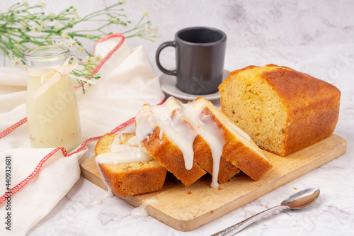 Sliced pound cake topped with lemon glaze on a cutting board and spoon are marble table.