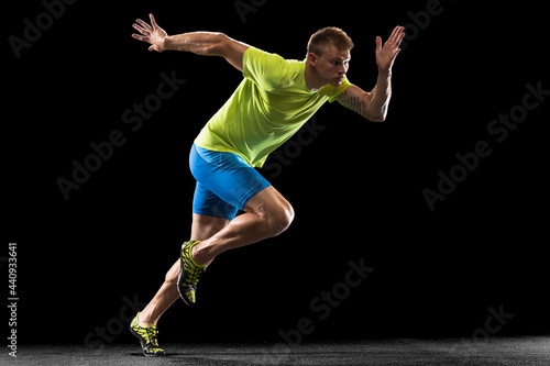 Caucasian professional male athlete, runner training isolated on black studio background. Muscular, sportive man. Concept of action, motion, youth, healthy lifestyle. Copyspace for ad. photo