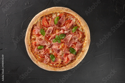 Pizza with tomatoes, prosciutto, basil on black background