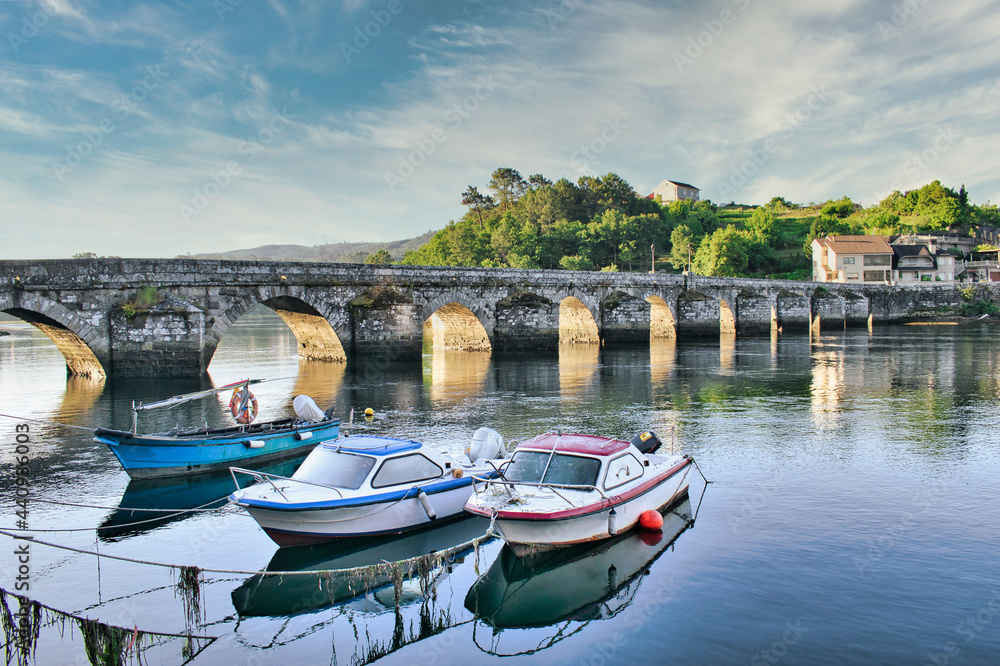 Barca y lanchas de pescador junto al puente medieval sobre el río Verdugo en Pontesampaio, Galicia, España