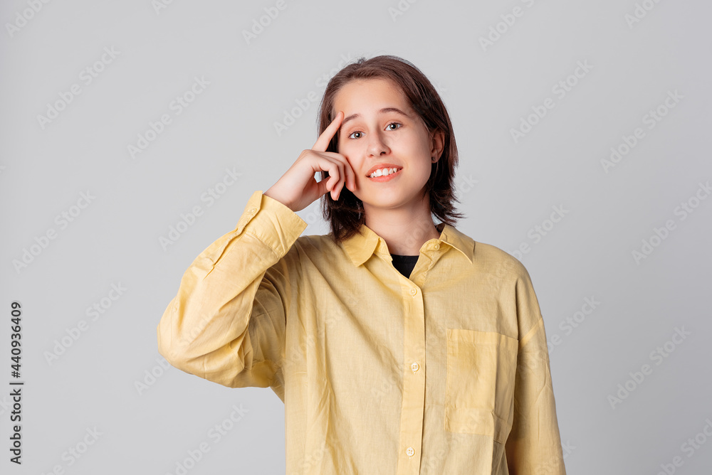 Confident teen girl pointing with finger at head, dressing in stylish yellow shirt. Concept of thinking. Be smart and think Confident teen girl pointing with finger at head, dressing in stylish yellow shirt. Concept of thinking. Be smart and think