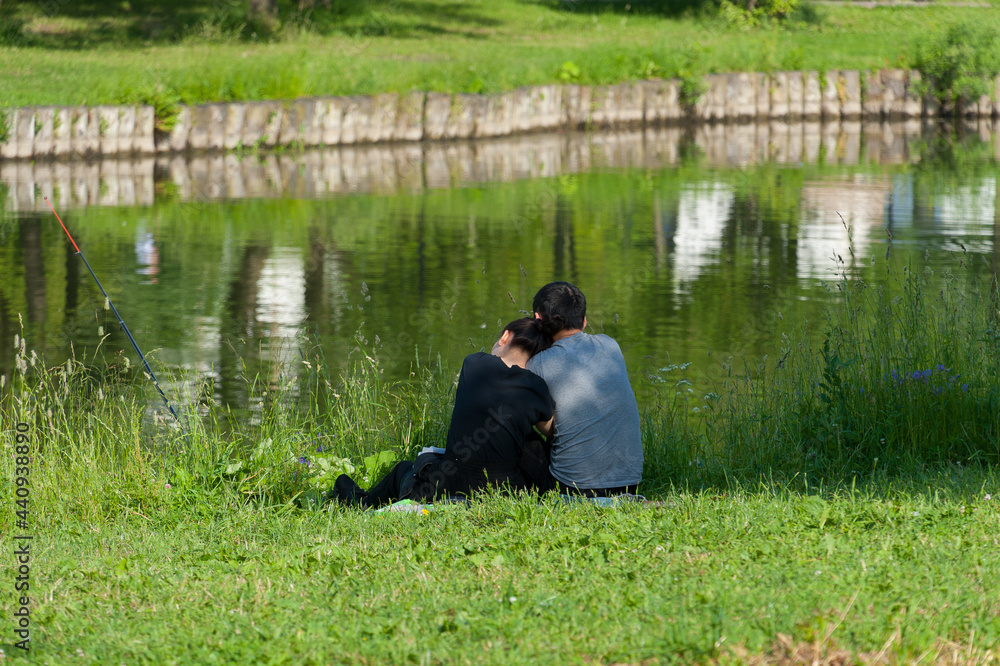 A couple in love is sitting on the shore of a pond and fishing A couple in love is sitting on the shore of a pond and fishing