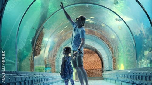 Child with his father watching underwater sea inhabitants in huge aquarium tunnel, Girl on dad hands learn about fishes and marine life. Family trip