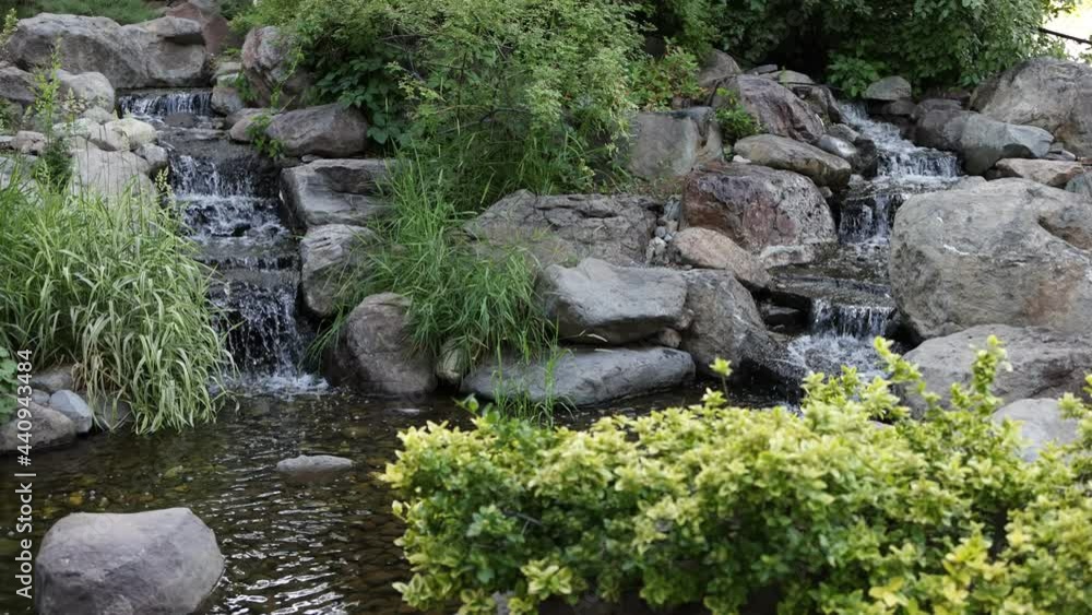 Two Small Waterfalls Flow into Pond in Park - Shallow Depth of Field - Slow Motion Two Small Waterfalls Flow into Pond in Park - Shallow Depth of Field - Slow Motion