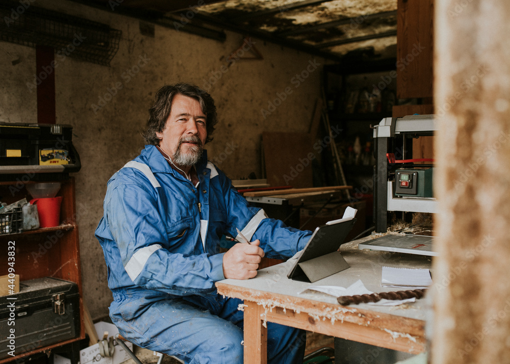 Senior carpenter writing on his notebook with laptop on the desk small business concept.. Senior carpenter writing on his notebook with laptop on the desk small business concept..