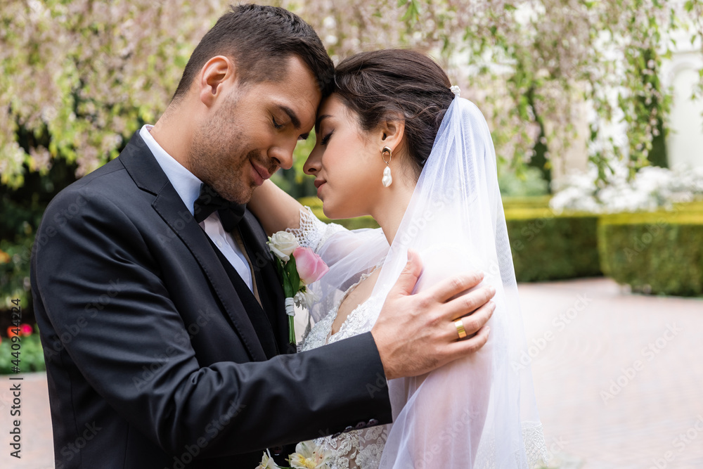 Side view of groom embracing young bride with closed eyes in park Side view of groom embracing young bride with closed eyes in park