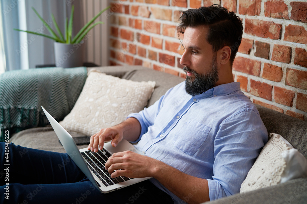 Man in a shirt sitting on couch and using laptop