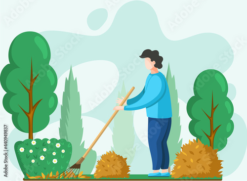 Young man doing seasonal garden work, remove leaves with rake, works on yard with trees. Agricultural worker in autumn tidies up garden, removes fallen yellow leaves stands near trees and bushes