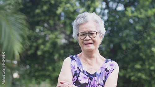 Beautiful senior woman with short gray hair smiling and looking at the camera while standing in a garden. Space for text. Aged people and relaxation concept.