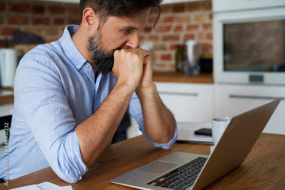 Stressed man sitting in front of a laptop at home Stressed man sitting in front of a laptop at home