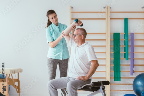 Physiotherapist assisting a senior patient performing weight exercises photo