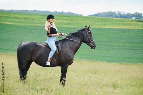 Young woman riding a horse on the green field