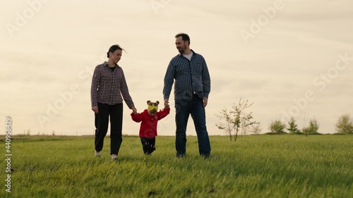 Dad and Mom daughter are playing on the field, the child is holding parents by hands. Happy family walks in the park holding hands in the summer at sunset. Teamwork. Happy childhood, family education