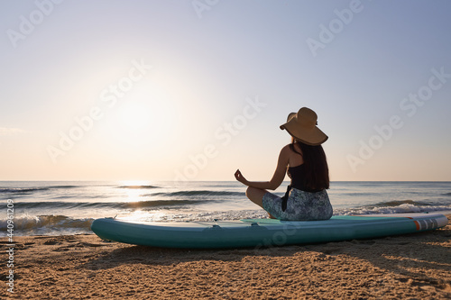 Young woman sitting on a paddle board with a relaxing posture at sunrise on the beach