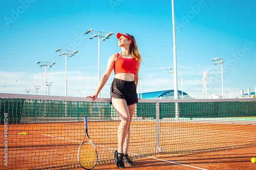 A beautiful woman rests after a workout. Tennis court. A girl in a black and red suit, an active lifestyle. Fitness body. outdoors. portrait. Happiness, pleasure, smiles. grid, stadium © Valeriia