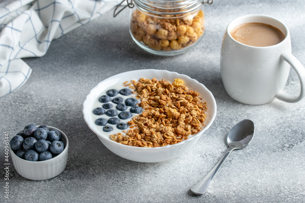 Granola with yogurt and coffee on a gray table. Hot morning drink. Muesli and blueberries in a white bowl. Dry breakfast concept. Healthy vegetarian food. Fitness diet. Granola with yogurt and coffee on a gray table. Hot morning drink. Muesli and blueberries in a white bowl. Dry breakfast concept. Healthy vegetarian food. Fitness diet.