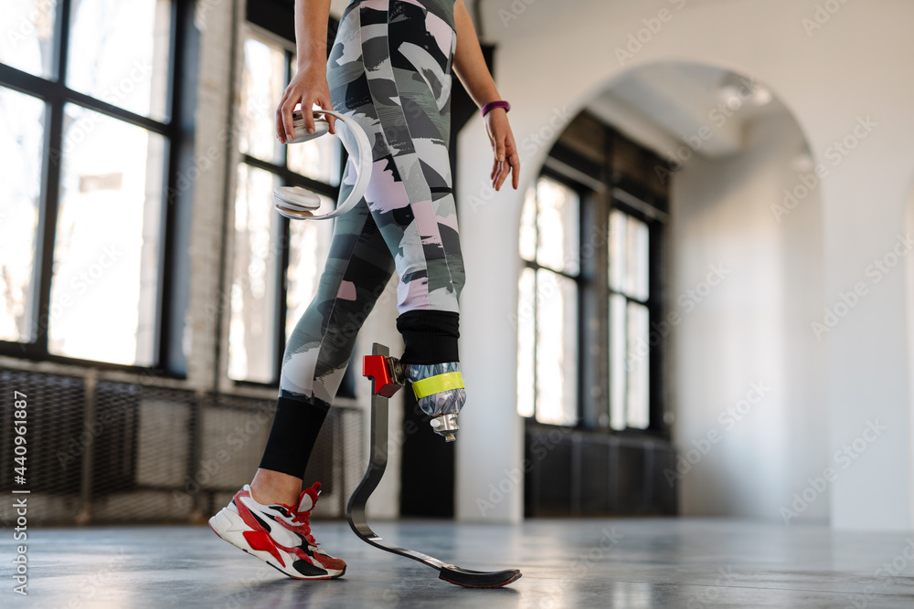 Obraz premium Young sportswoman with prosthesis holding headphones while working out