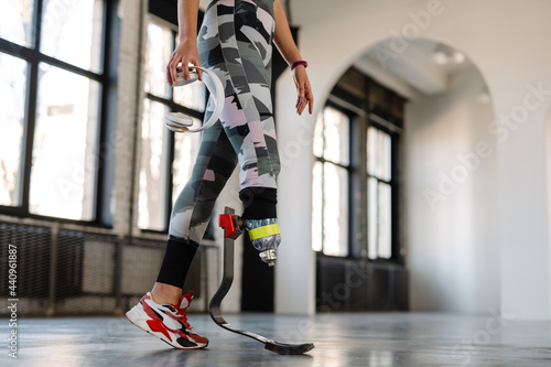 Young sportswoman with prosthesis holding headphones while working out