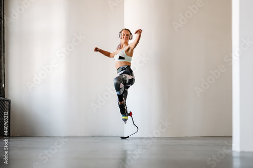 Young sportswoman with prosthesis listening music and dancing indoors