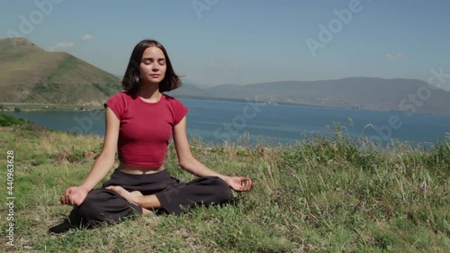 Relaxed woman doing yoga in nature and sitting in Lotus pose during meditation in mountains on sunny day  photo