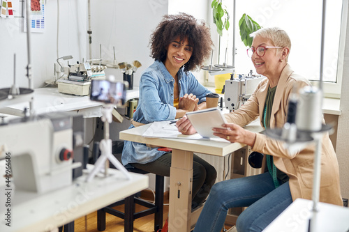 Woman designer and African-American assistant look at modern sewing machine in workshop