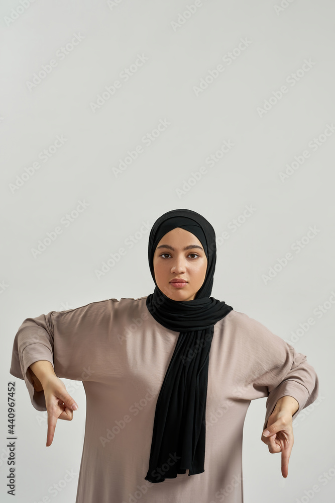 Calm young arabic woman in hijab pointing fingers down Calm young arabic woman in hijab pointing fingers down