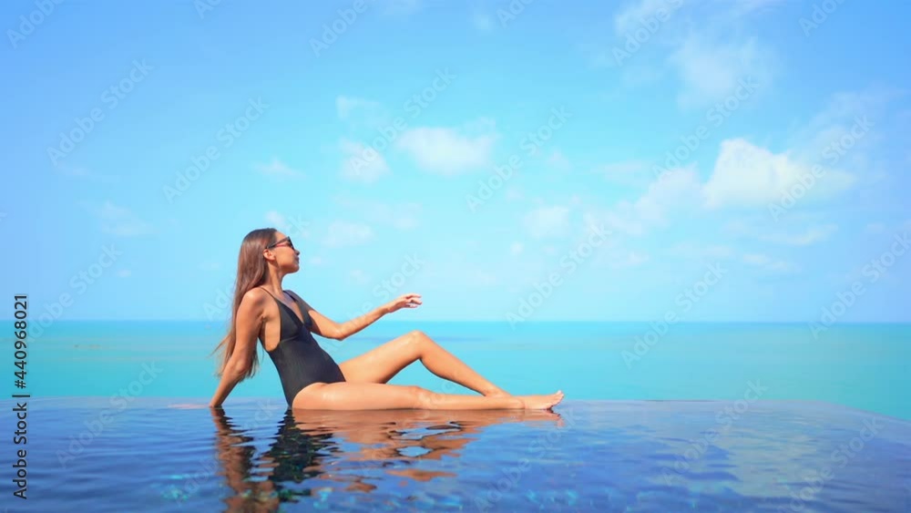 Sexy exotic female in swimsuit sitting on infinity pool edge enoying in stunning view of tropical sea horizon, slow motion Sexy exotic female in swimsuit sitting on infinity pool edge enoying in stunning view of tropical sea horizon, slow motion