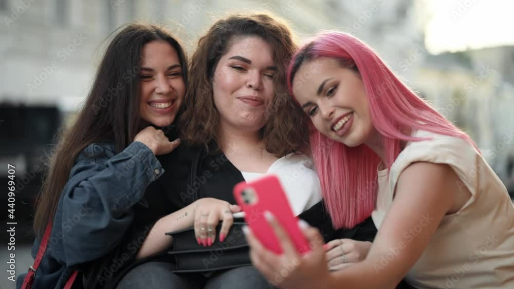 A smiling disabled woman is sitting on the wheelchair while spending time with her friends and taking selfie photo on the city street