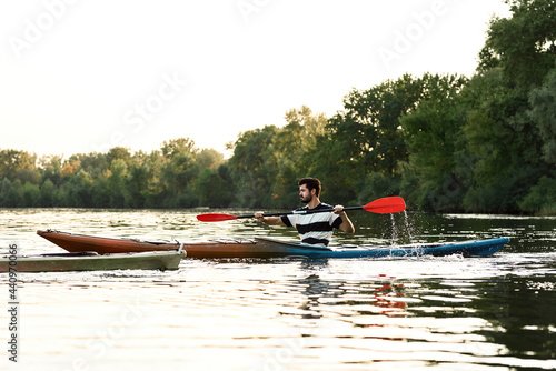 Active young caucasian guy looking concentrated while boating on a lake surrounded by peaceful nature