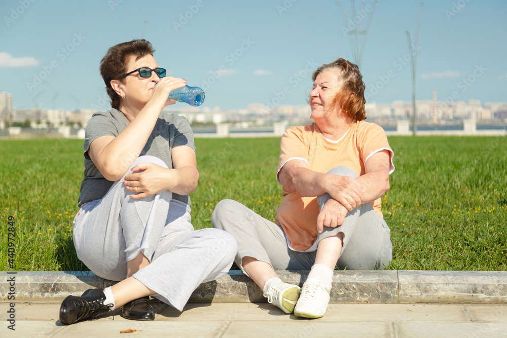 Two pensioner woman resting after training in the park. Fitness training for aged people. Healthy lifestyle concept. Two pensioner woman resting after training in the park. Fitness training for aged people. Healthy lifestyle concept.