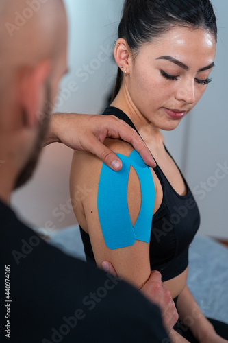 Physical therapist applying kinesiology tapes on shoulder of sportswoman