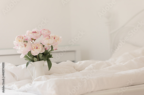 Bouquet of pink peonies on white bed linen. Modern interior in the bedroom. Wedding and festive style.
