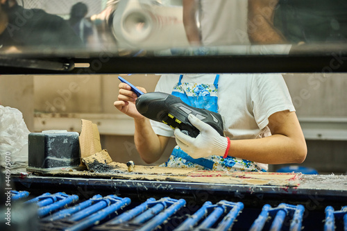 Detail of worker applying glue to the shoes sole in a production line