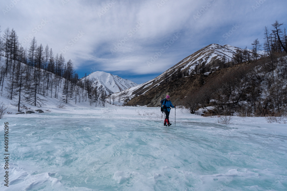 A girl walks along an icy river among the mountains